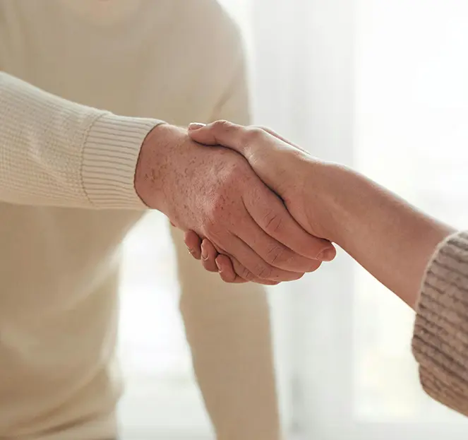 Two people shake hands across a table in an indoor setting.