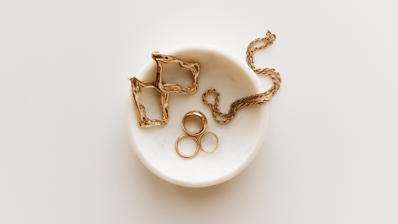 Minimalistic gold jewelry in a marble dish.