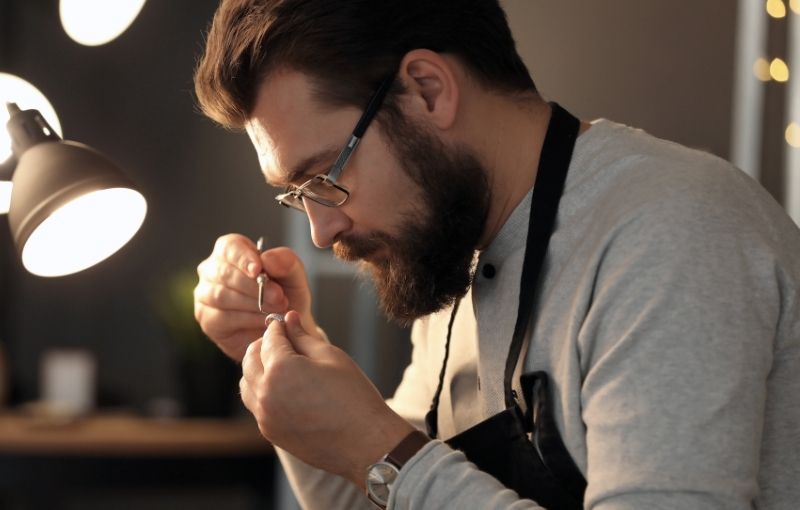 Artisan inspecting ring under lamp.