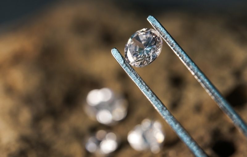 Diamond held by tweezers outdoors.