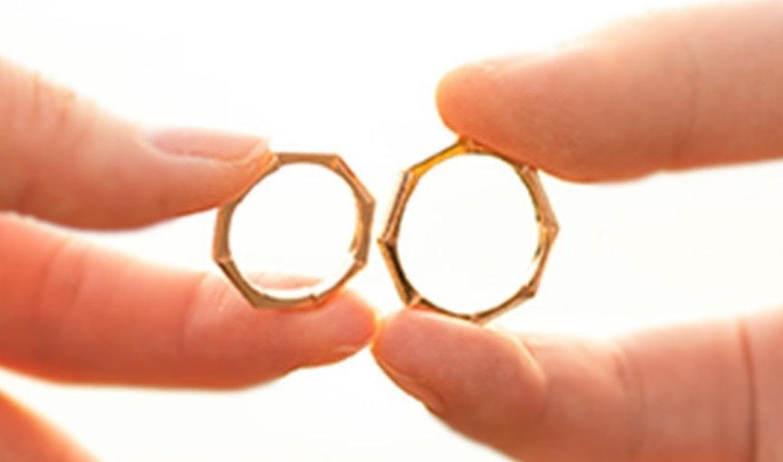 Close-up hands holding matching geometric gold rings