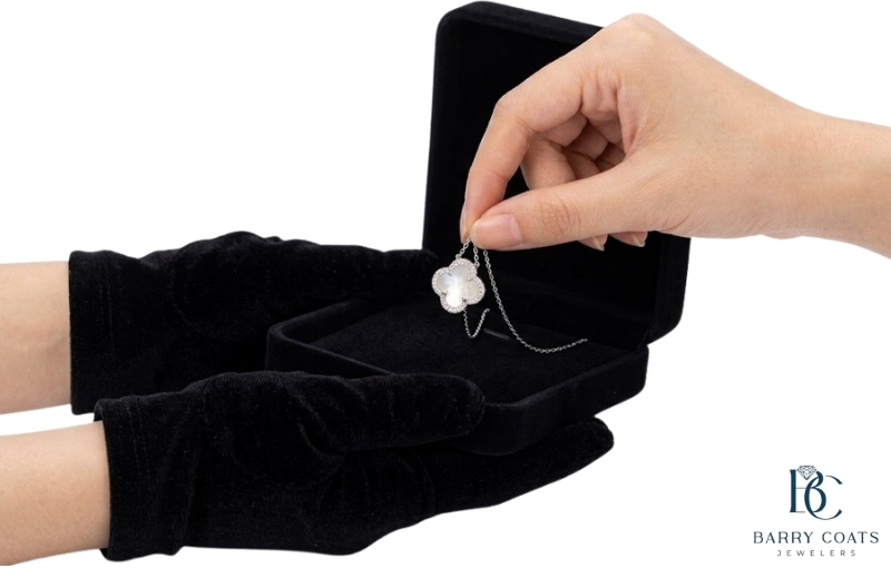 White clover pendant necklace held over jewelry box Diamond pavé wedding band on bride's hand