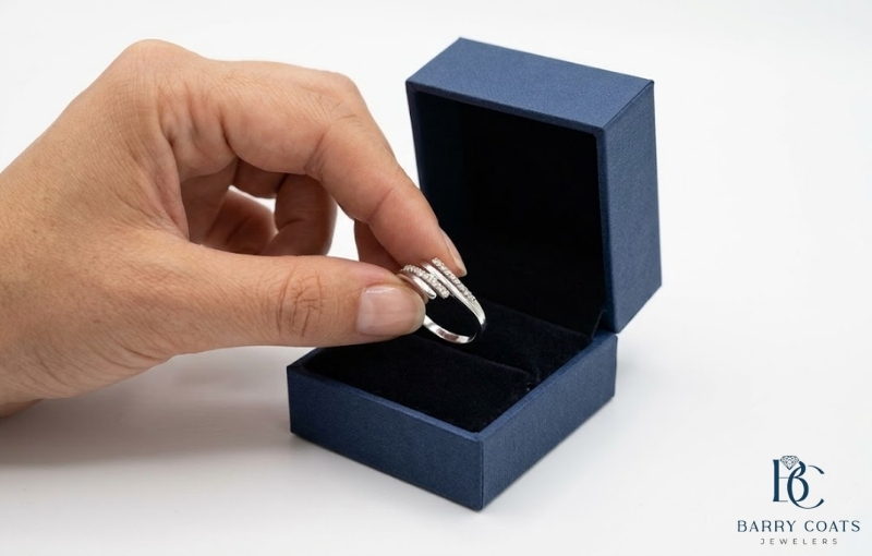 A hand holding a silver ring over a blue box Diamond pavé wedding band on bride's hand